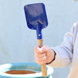 A child holding a Glückskäfer Square Metal Blue Shovel in their hand.