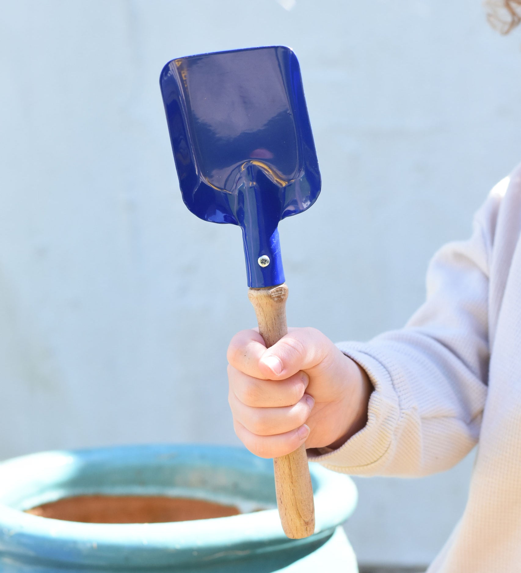 A child holding a Glückskäfer Square Metal Blue Shovel in their hand.