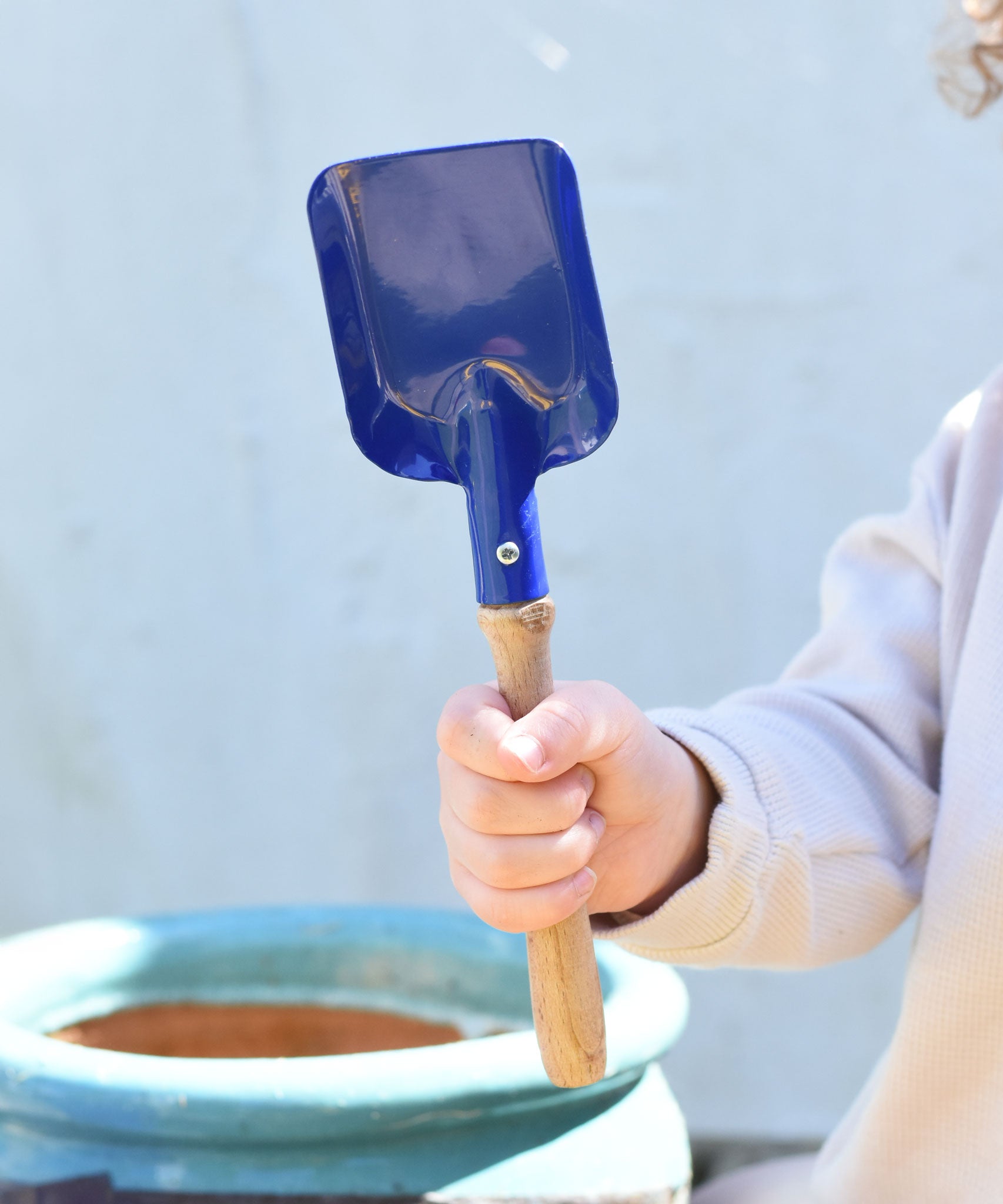 A child holding a Glückskäfer Square Metal Blue Shovel in their hand.