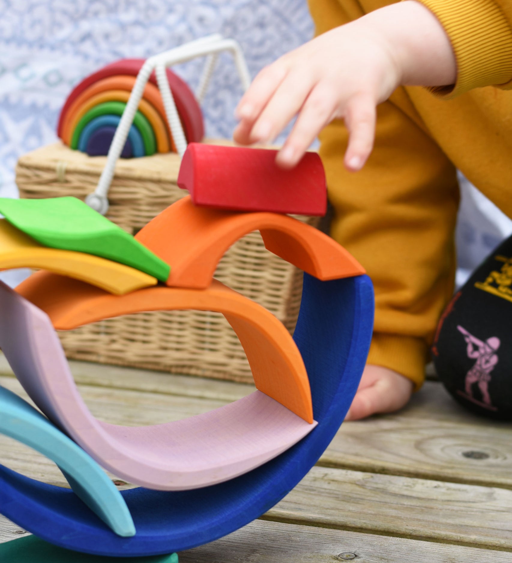 A close up of a child's hand placing a piece of the Glückskäfer Blue Sunrise Set on a stack.