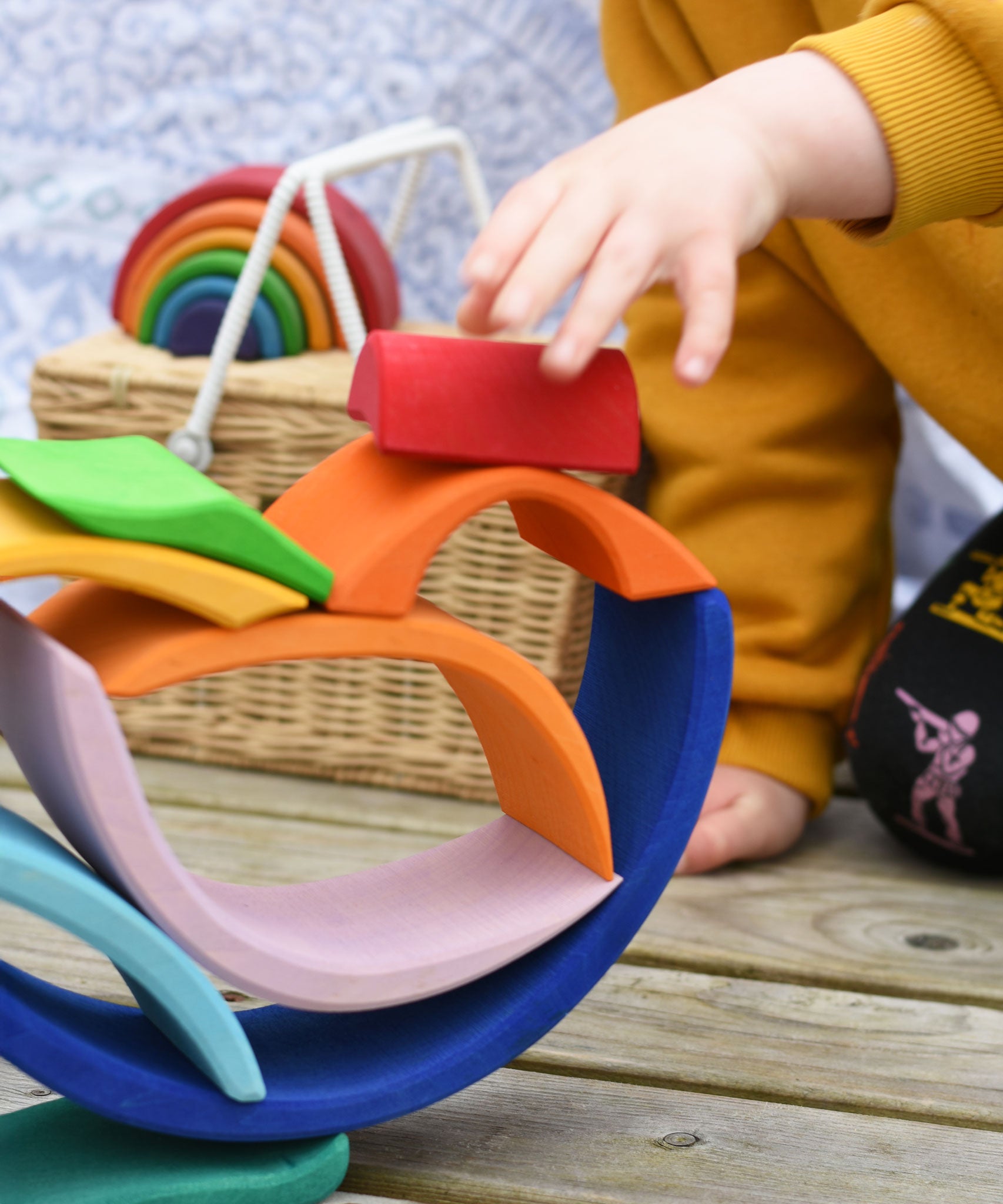 A close up of a child's hand placing a piece of the Glückskäfer Blue Sunrise Set on a stack.