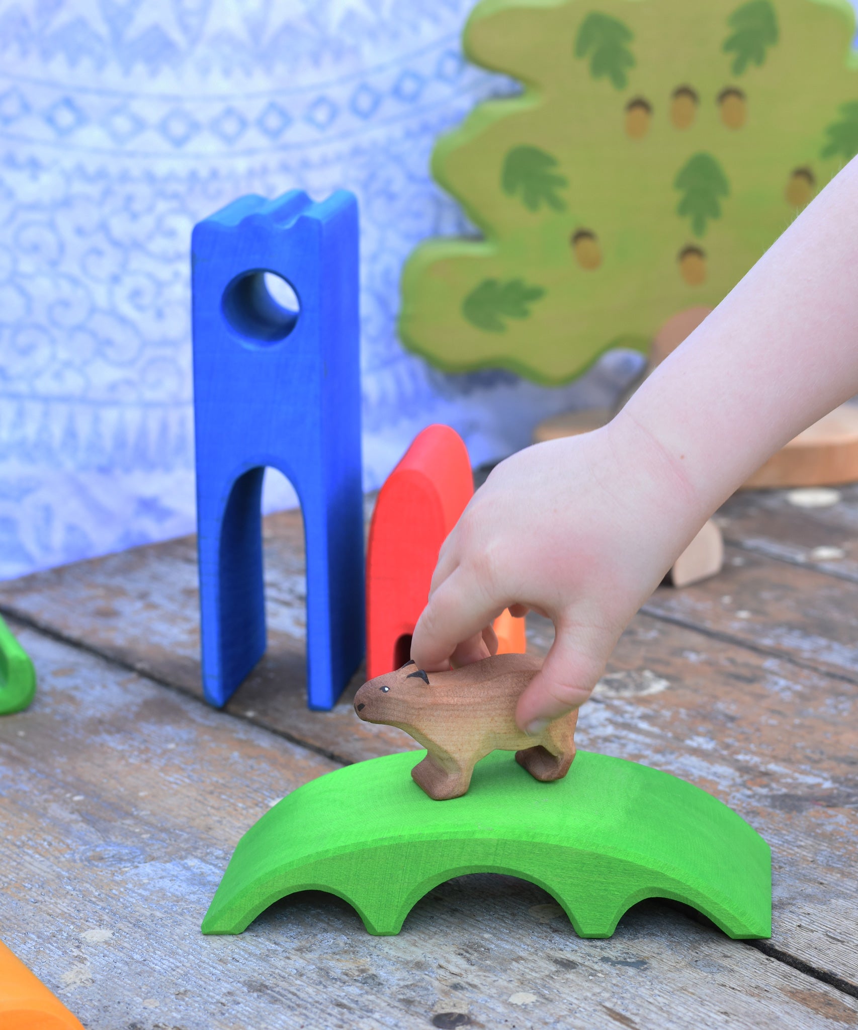 A child's hand placing a Bumbu Capybara on the green coloured bridge piece from the Gluckskafer Castle set. 