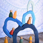 The arches from the Glückskäfer Blue Grotto set tacked on top of each other with Graapt wooden Nin peg dolls placed on and underneath the stack.
