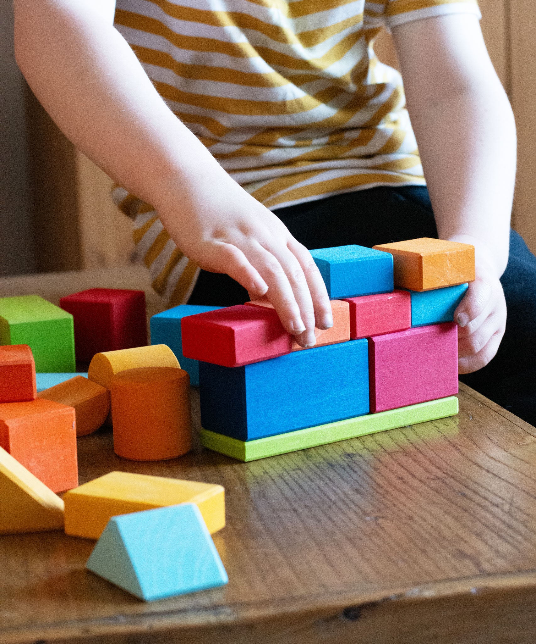 A child stacking blocks from the Glückskäfer 27 Piece Building Blocks Set on top of each other. 