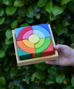 Glückskäfer circles quadrat construction kit in a wooden tray in a child's hand.