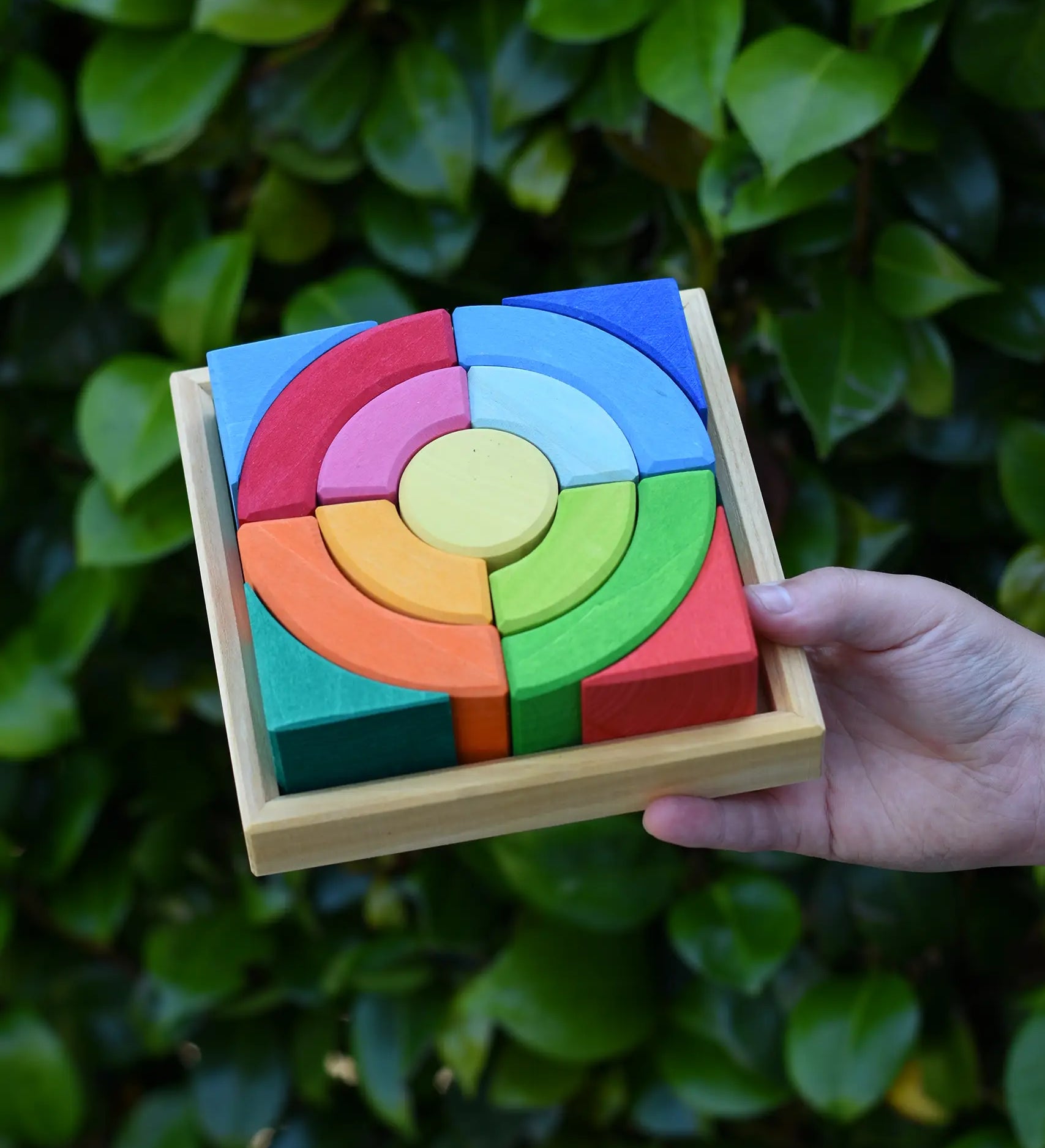 Glückskäfer circles quadrat construction kit in a wooden tray in a child's hand.