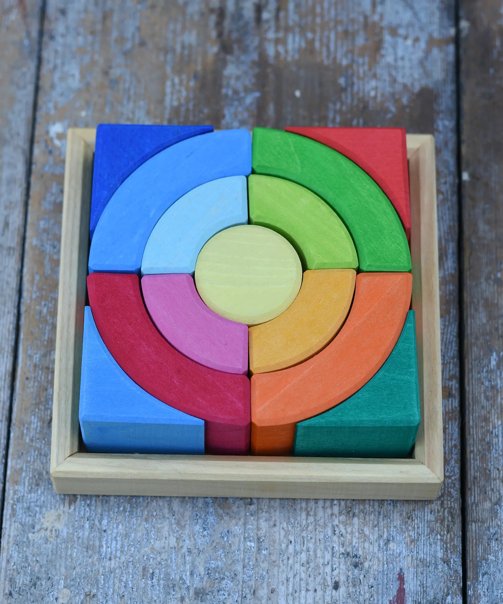 Glückskäfer circles quadrat construction kit in a square display tray placed on a wooden desk. 