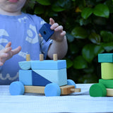 Child playing with the Glückskäfer colourful shape train wooden toy with a blue block in his hand.