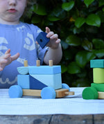 Child playing with the Glückskäfer colourful shape train wooden toy with a blue block in his hand.