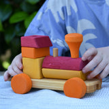 Child playing with the Glückskäfer colourful shape train wooden toy pushing the red and orange carriage along.