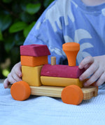 Child playing with the Glückskäfer colourful shape train wooden toy pushing the red and orange carriage along.