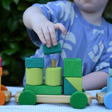 Child playing with the Glückskäfer colourful shape train wooden toy placing a square block on the pillar on the base piece.