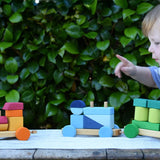 Child pointing at the Glückskäfer colourful shape train wooden toy placed on a wooden table outdoors.