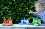 Child pointing at the Glückskäfer colourful shape train wooden toy placed on a wooden table outdoors.