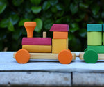 Close up of the red and orange carriage onthe Glückskäfer colourful shape train wooden toy placing a square block on the pillar on the base piece.