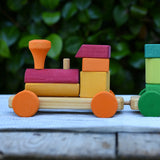 Close up of the red and orange carriage onthe Glückskäfer colourful shape train wooden toy placing a square block on the pillar on the base piece.