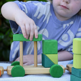 Child playing with the Glückskäfer colourful shape train wooden toy placing a green block on the pillars of the base piece.
