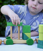 Child playing with the Glückskäfer colourful shape train wooden toy placing a green block on the pillars of the base piece.