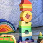 The Glückskäfer Crooked Tower set on a wooden surface surrounded by other wooden toys. 