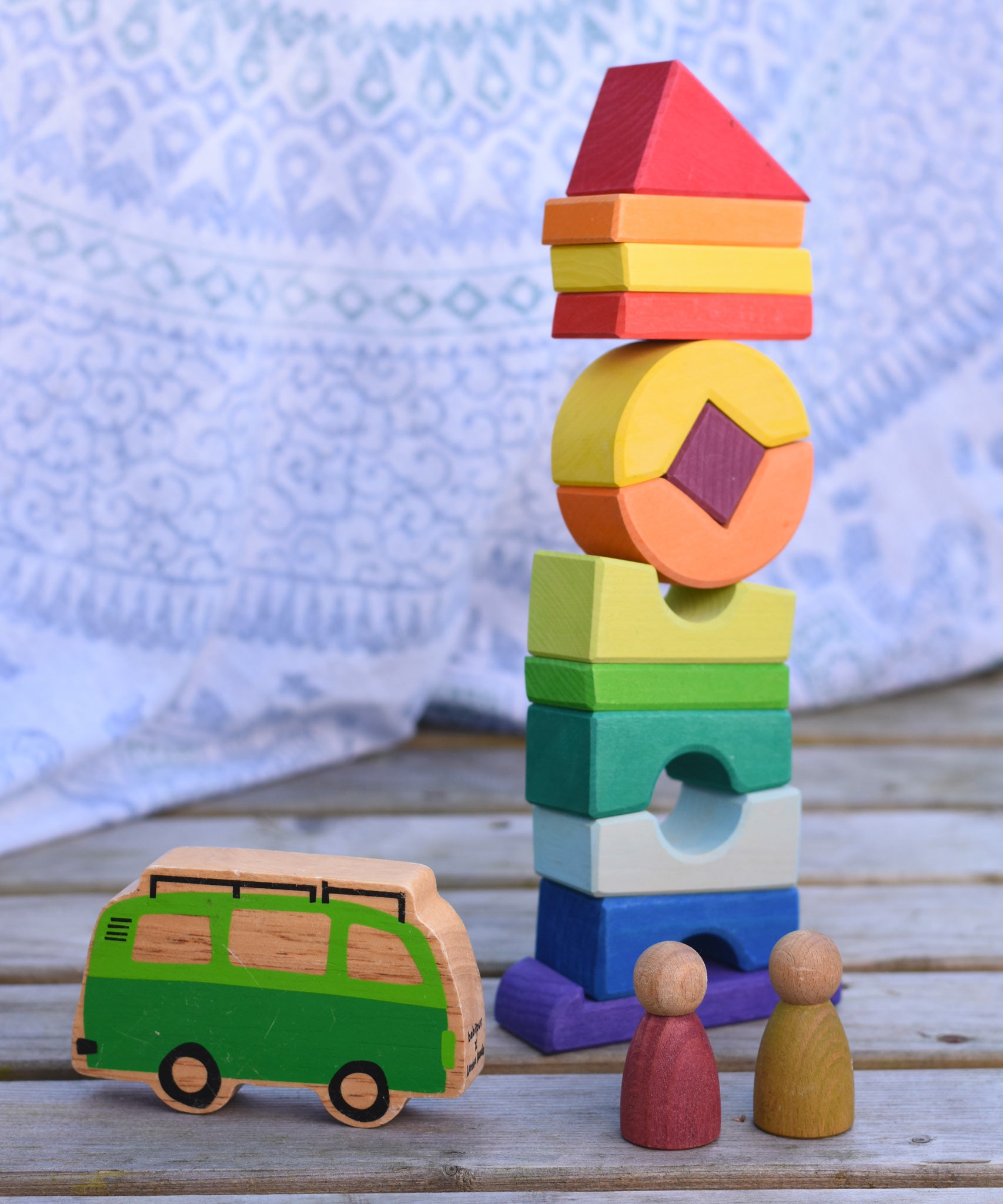 The Glückskäfer Crooked Tower placed on a wooden surface with a Lanka Kade camper van toy and Grapat Nins in front of it. 