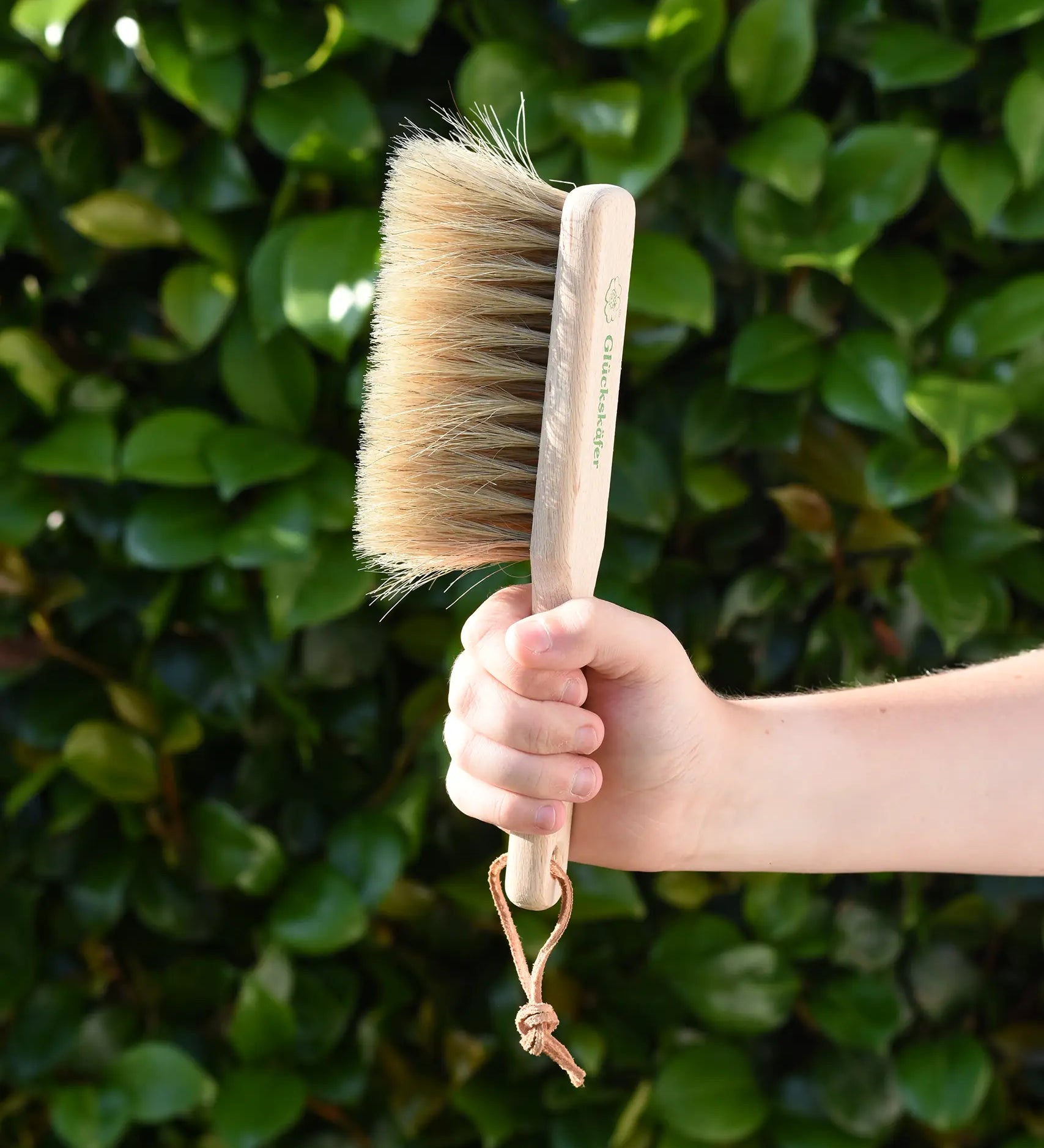 Glückskäfer wooden dust brush with natural horse hair bristles in a child's hand.