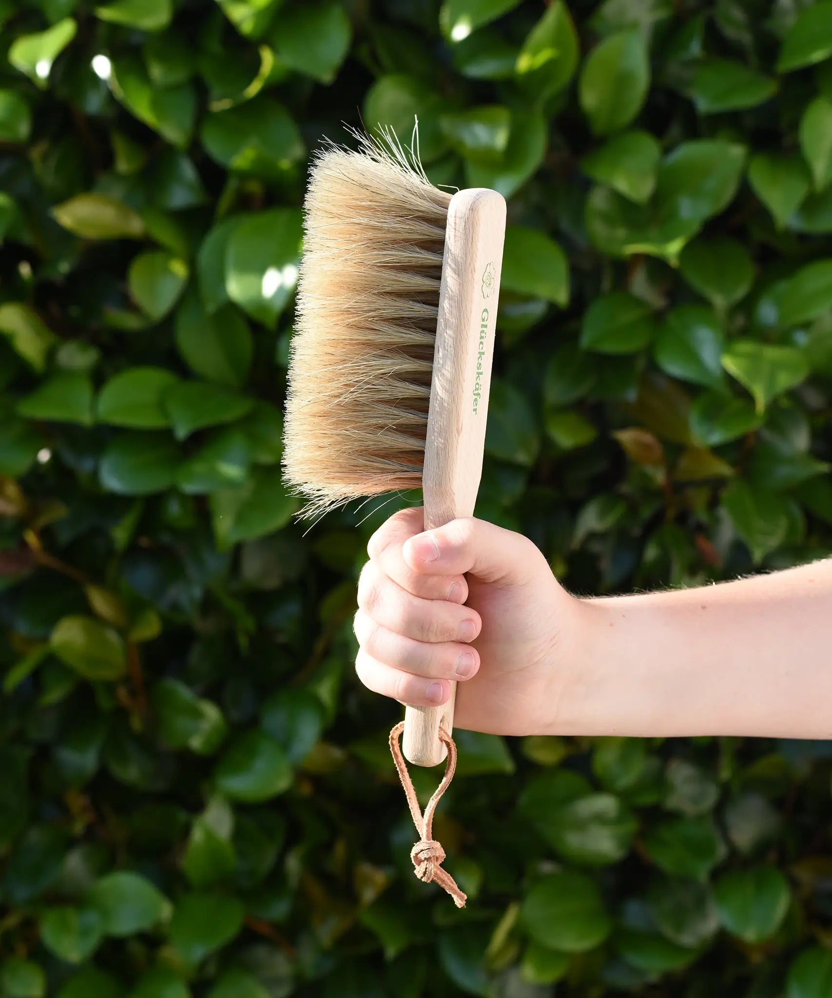 Glückskäfer wooden dust brush with natural horse hair bristles in a child's hand.
