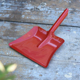 Glückskäfer red metal dust pan placed on a wooden surface.