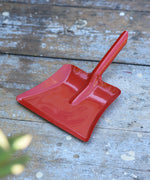 Glückskäfer red metal dust pan placed on a wooden surface.