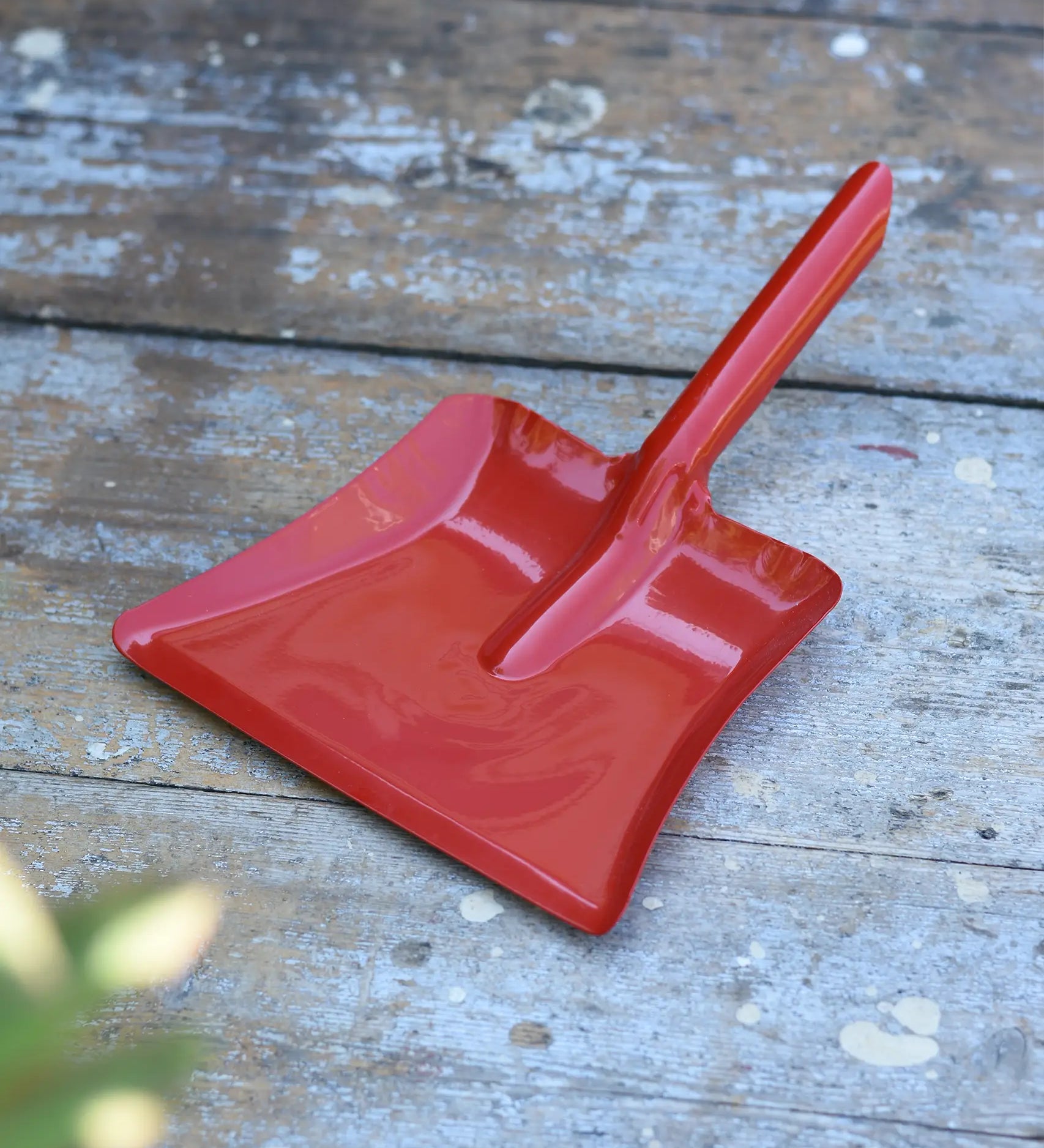 Glückskäfer red metal dust pan placed on a wooden surface.