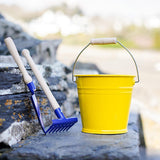 A yellow Gluckskafer bucket pictured outdoors on slate steps with a blue metal spade and rake next to them