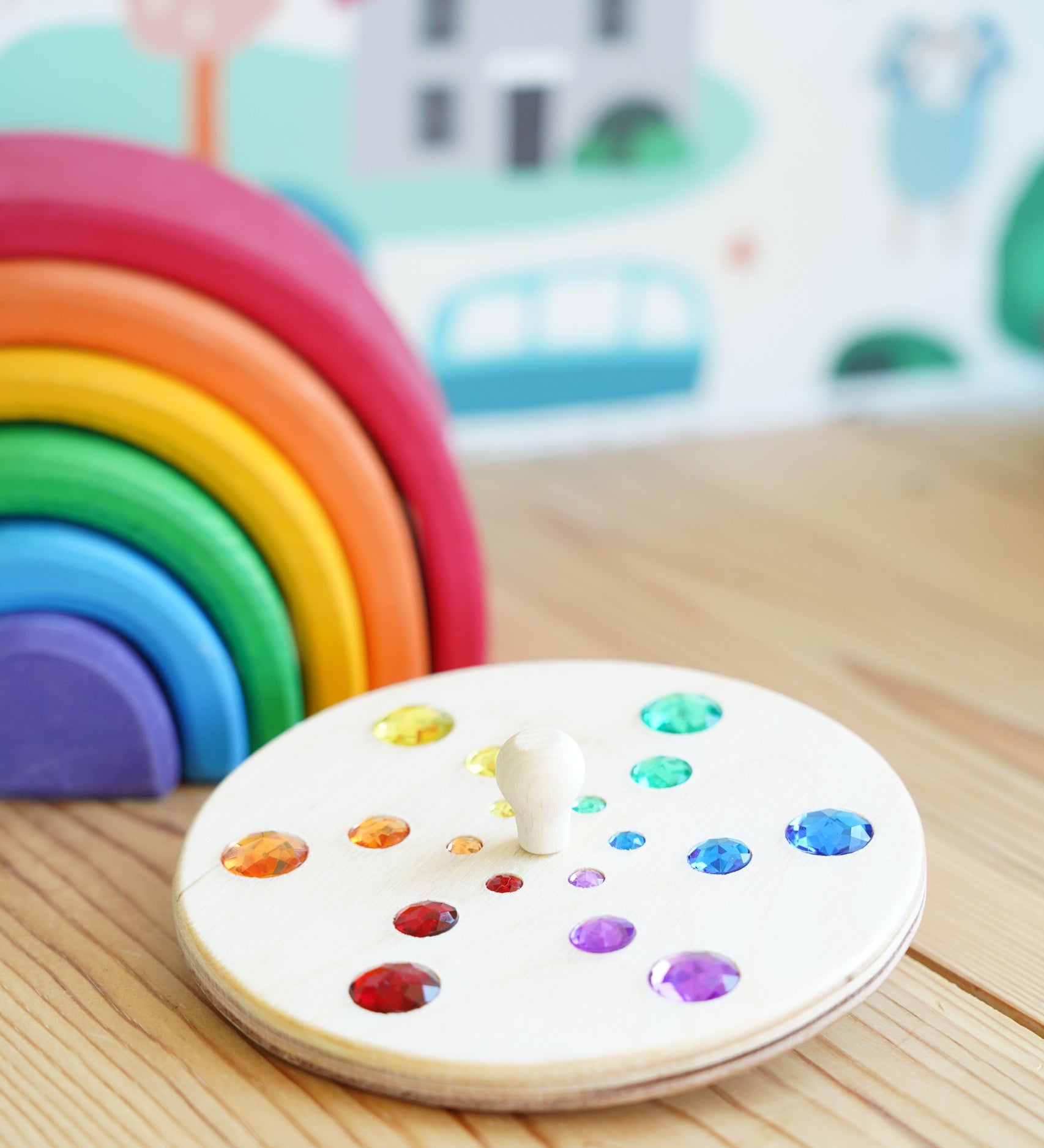 Glückskäfer Fantasy Sparkling Spinning Top placed on a wooden windowsill next to a Grimm's 6 piece rainbow.