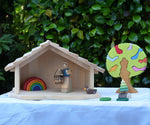 Gluckskafer farm & nativity stable wooden toy building with an Ostheimer doll and Grimm's mini rainbow placed inside next to a Gluckskafer bird tree.