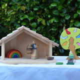 Gluckskafer farm & nativity stable wooden toy building with an Ostheimer doll and Grimm's mini rainbow placed inside next to a Gluckskafer bird tree.