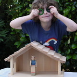 Child standing behind the Gluckskafer farm & nativity stable wooden toy building with Grapat rings held up to his eyes. 
