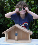 Child standing behind the Gluckskafer farm & nativity stable wooden toy building with Grapat rings held up to his eyes. 