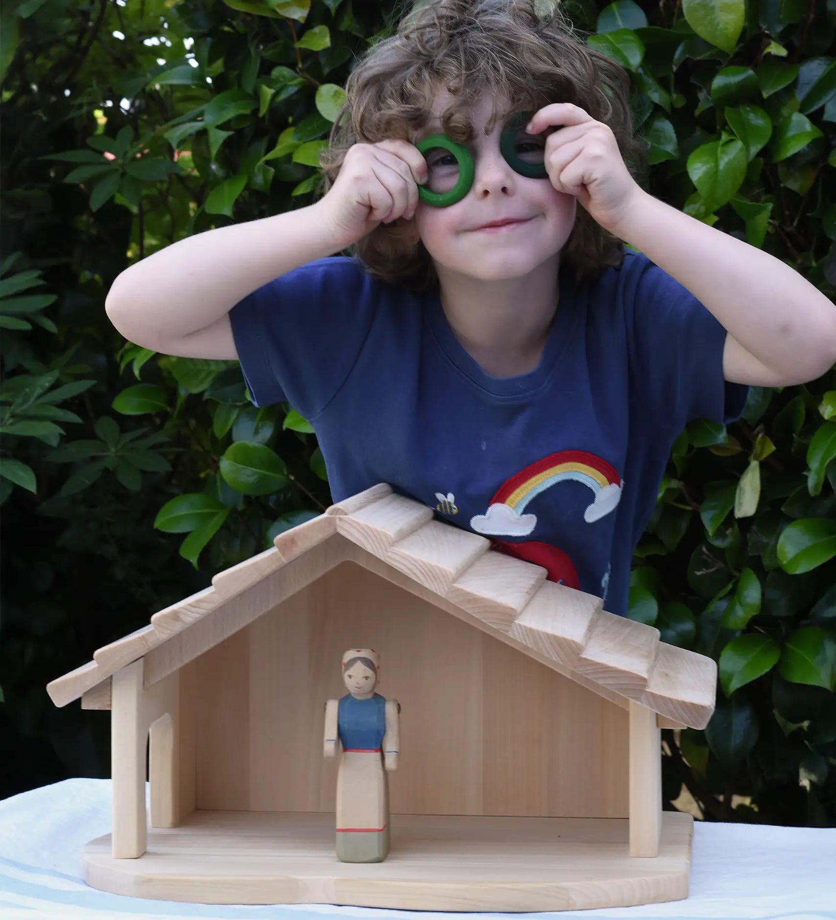 Child standing behind the Gluckskafer farm & nativity stable wooden toy building with Grapat rings held up to his eyes. 