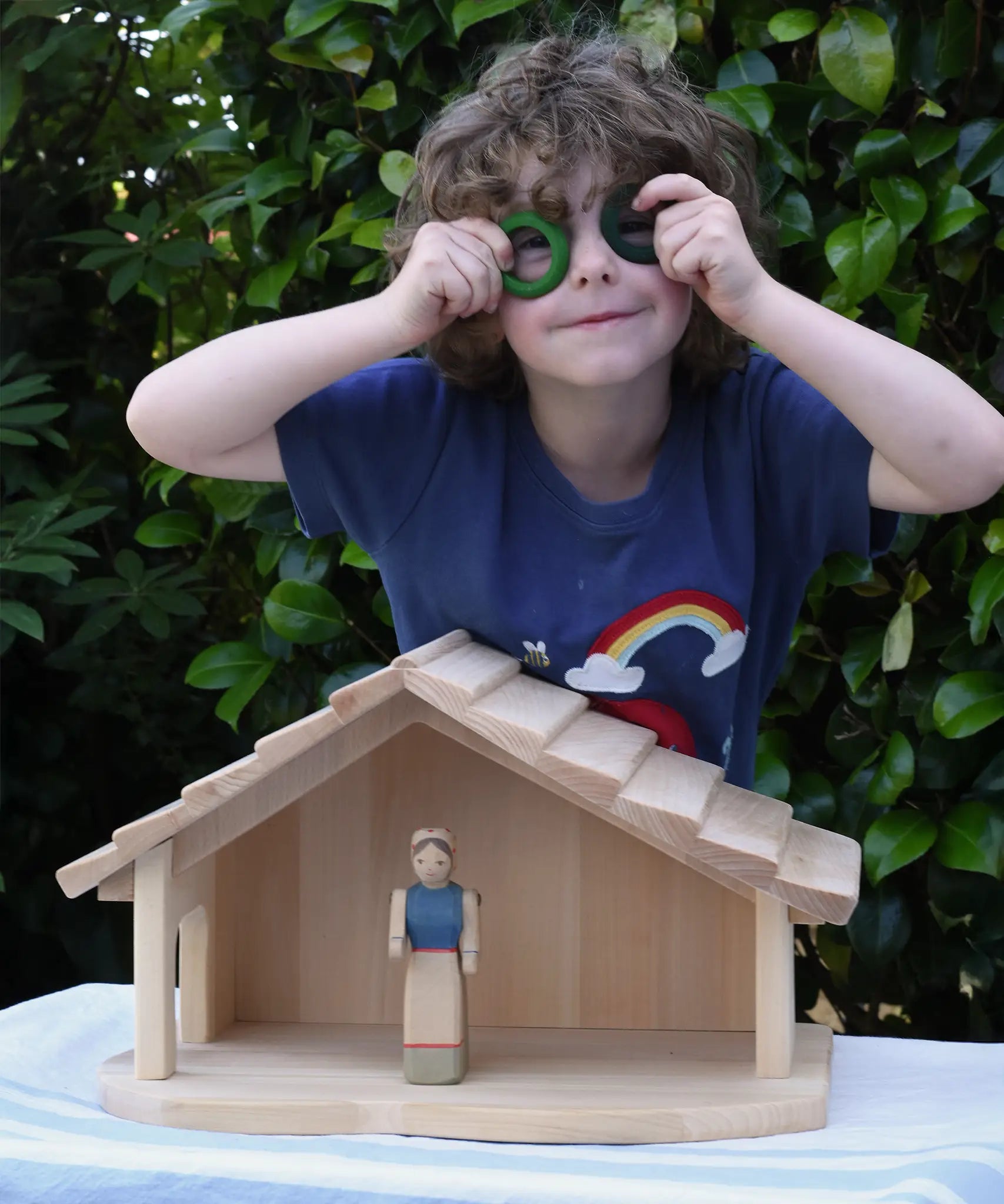 Child standing behind the Gluckskafer farm & nativity stable wooden toy building with Grapat rings held up to his eyes. 
