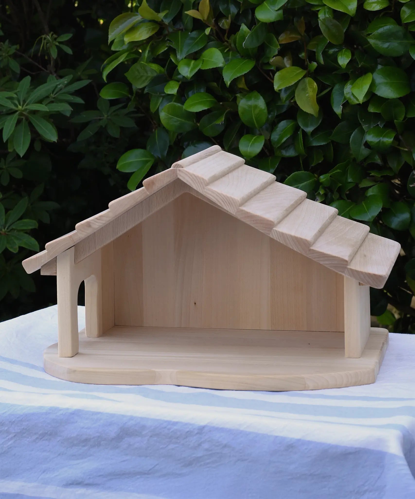 Gluckskafer farm & nativity stable wooden toy building placed on a cloth covered table outdoors.