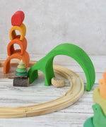 The largest pieces from the Glückskäfer Green 8 Piece Arch House set shown placed over a wooden toy train track to use as a tunnel.