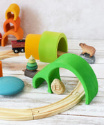 The largest pieces from the Glückskäfer Green 8 Piece Arch House set shown placed over a wooden toy train track to use as a tunnel. The smaller arch pieces can be seen on the track in the background. 
