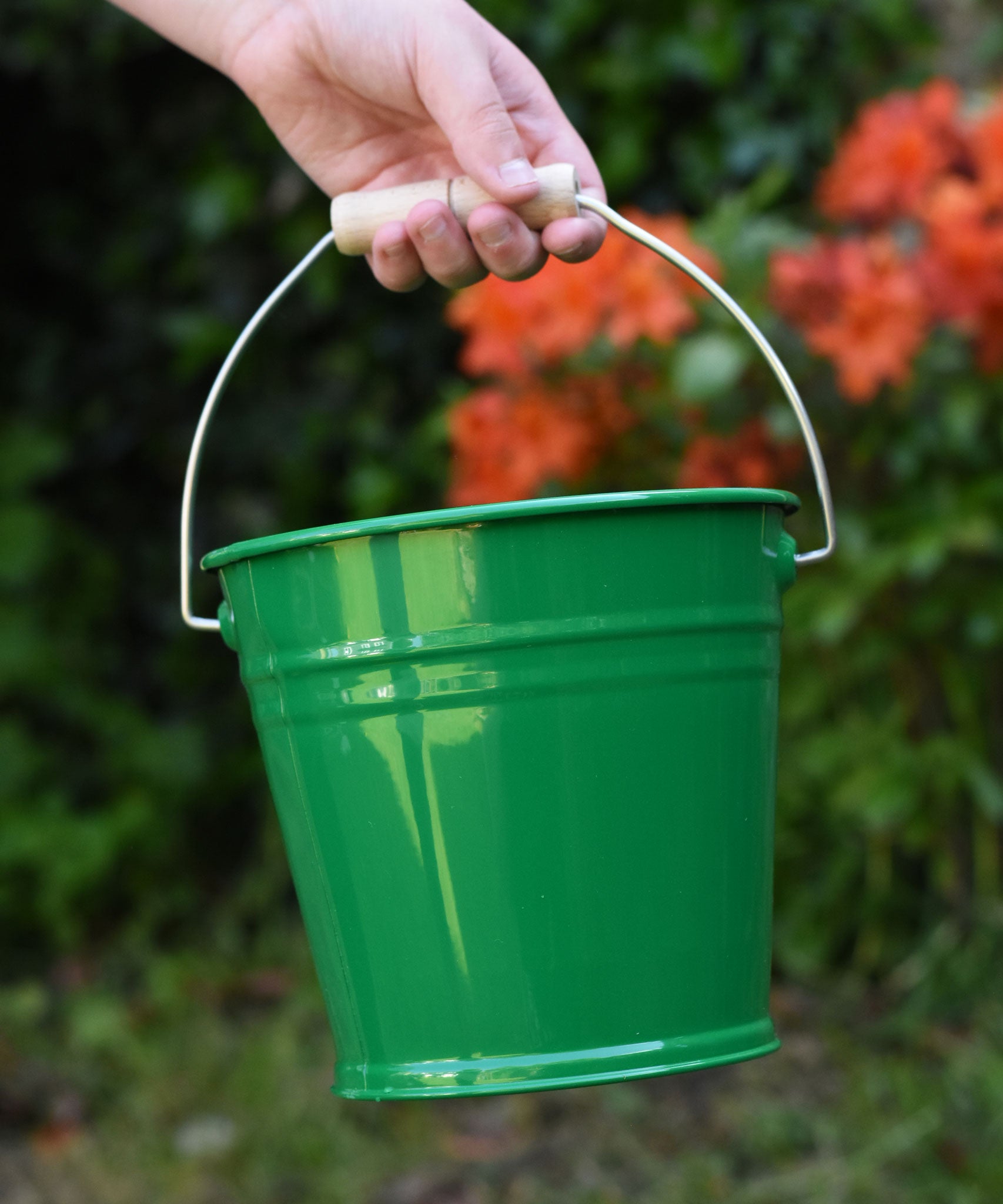 A close up of a Glückskäfer Green Metal Bucket in a child's hand. 