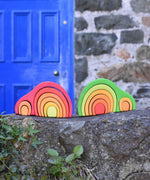 The red and green Glückskäfer Green 8 Piece Arch Houses placed on a stone wall in front of a blue doors outdoors. 