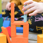 A close up of a child's hand using blocks from the Glückskäfer 29-Piece House Blocks set to create a tower.