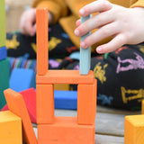 A close up of a child's hand using blocks from the Glückskäfer 29-Piece House Blocks set to create a tower.