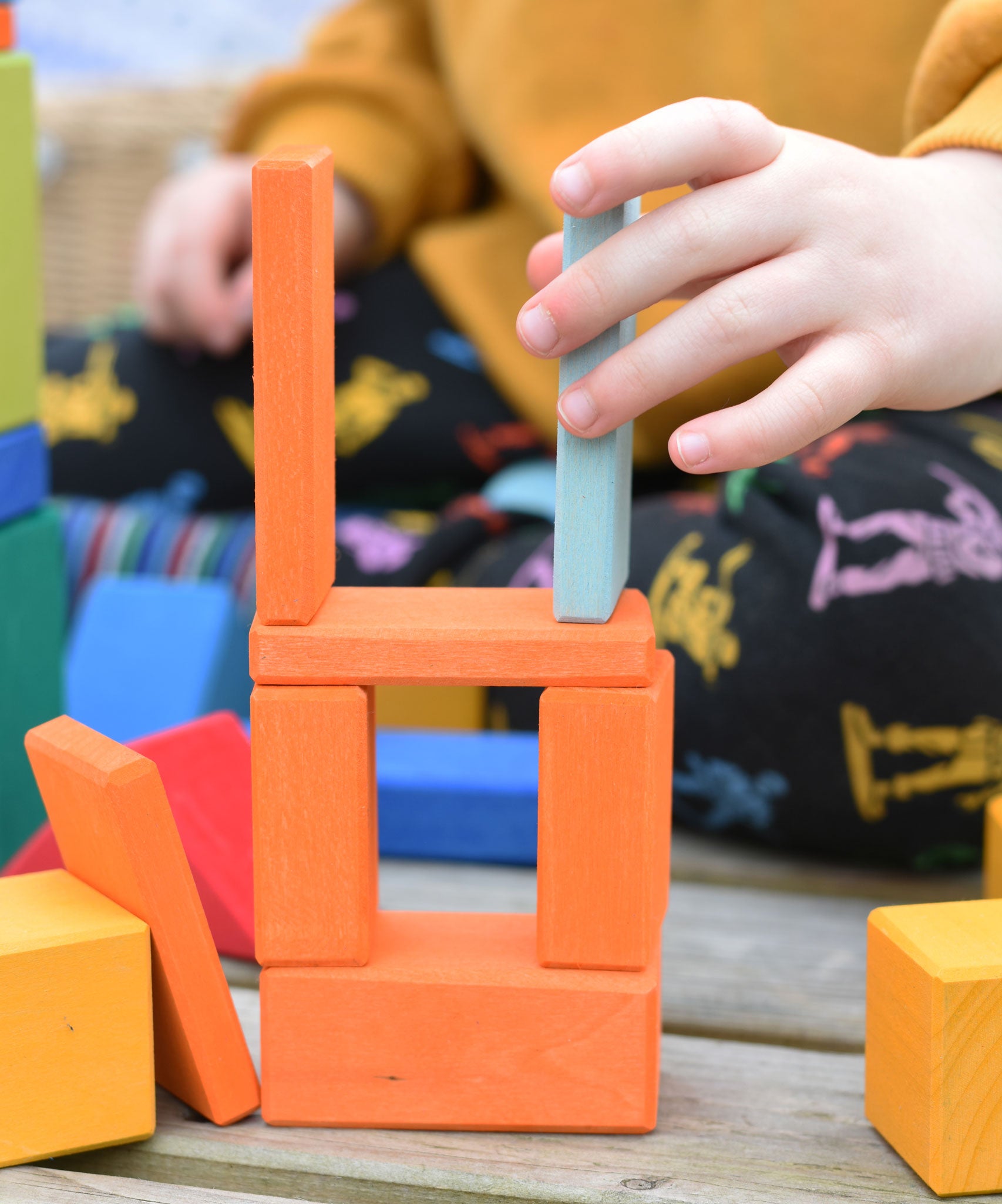 A close up of a child's hand using blocks from the Glückskäfer 29-Piece House Blocks set to create a tower.