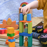 A child placing a Grimm's friend on a tower they have created using blocks from the Glückskäfer 29-Piece House Blocks.