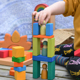 A child placing a Grimm's friend on a tower they have created using blocks from the Glückskäfer 29-Piece House Blocks.