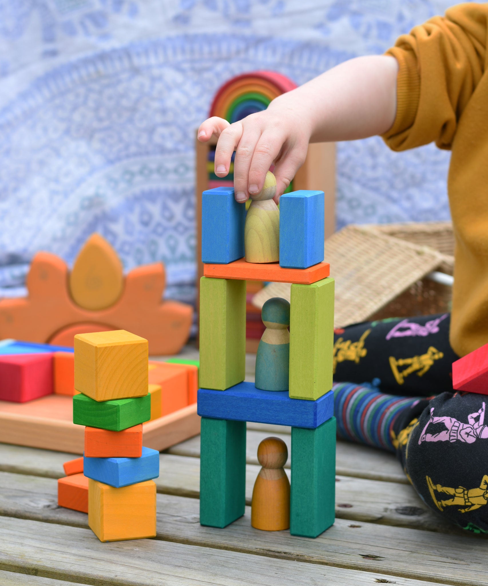 A child placing a Grimm's friend on a tower they have created using blocks from the Glückskäfer 29-Piece House Blocks.