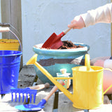 A child using a Glückskäfer Round Metal Red Shovel to prepare the soil in a pot ready to plant a Babipur seedbom in. Other Gluckskafer garden items such as a bucket and watering can can be seen at the front. 