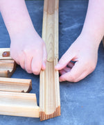 A close up of a child's hand laying out the Glückskäfer 23 Piece Wooden Marble Track laid out onto a slate surface outdoors. 